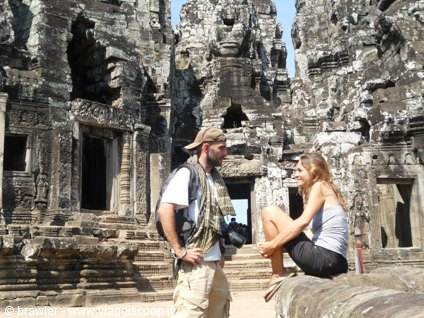 Two tourists beside the carved stone towers of Bayon, Angkor Thom