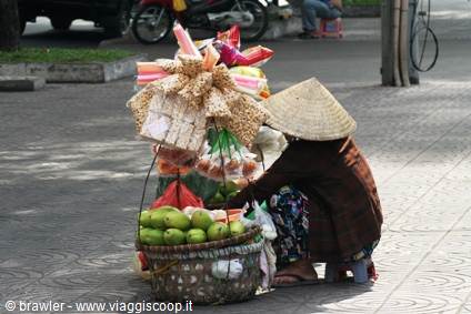 Street vendor in conical straw hat crouching beside fruit baskets