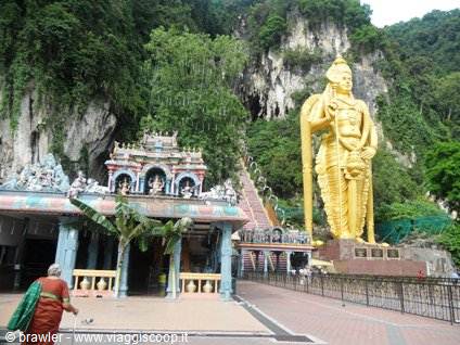 Golden Murugan statue at Batu Caves entrance beside a colorful Hindu temple
