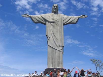 Christ the Redeemer stone statue with open arms, tourists below, blue cloudy sky