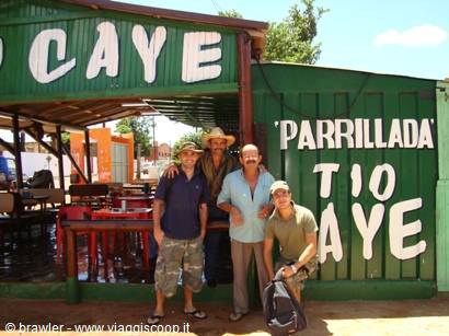 Four men pose in front of Tio Caye parrillada, a green wooden eatery