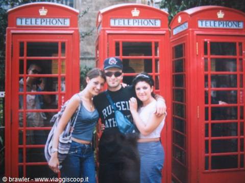 Three friends hugging in front of London's red telephone boxes