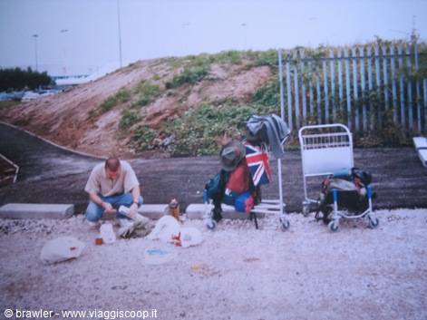 Traveler crouching with luggage and trolleys beside a metal fence