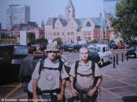Two backpackers with hiking packs walking on a street, brick buildings behind