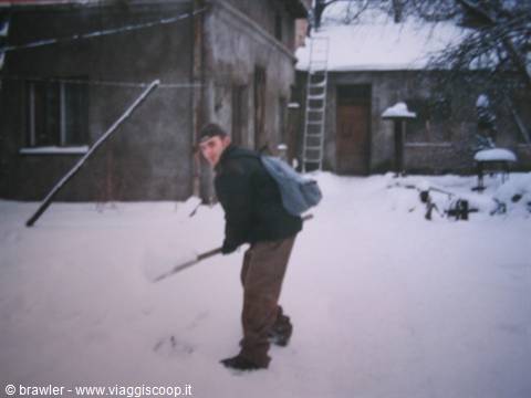 Young man with backpack shovels snow in front of a house