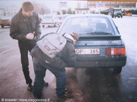 Backpacker leaning into the trunk of a parked grey Ford in a lot