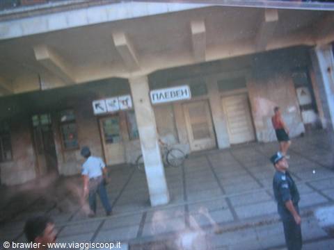 Uniformed officer and passersby outside a station pavilion with Cyrillic sign