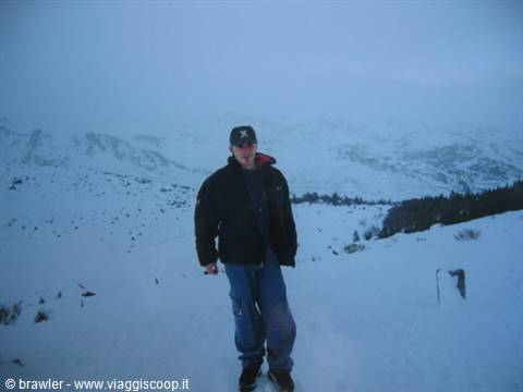 Young man in black hood standing on snow, foggy snowy mountains behind