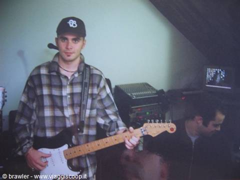 Young man in black cap and plaid shirt playing electric guitar in a rehearsal room