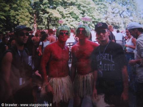 Two men with red-painted bodies, green wigs and straw skirts among the crowd