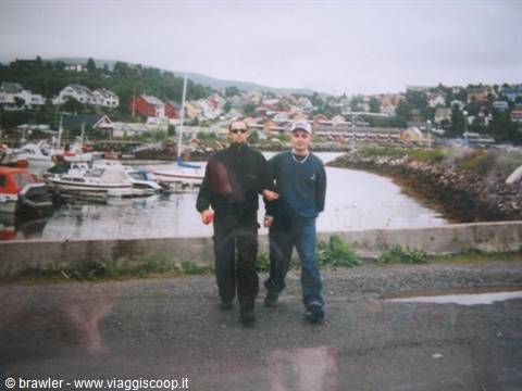 Two guys walk in front of the harbor with boats and colorful houses
