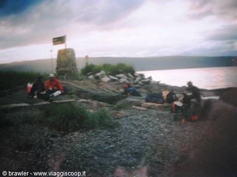 Cyclists resting on a pebble beach beside a stone cairn, cloudy sky