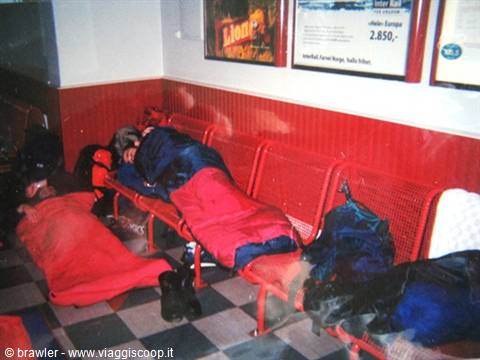Travelers in sleeping bags sleeping on red benches in a waiting room