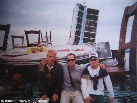 Three friends posing before giant table and chairs sculpture with tilted building