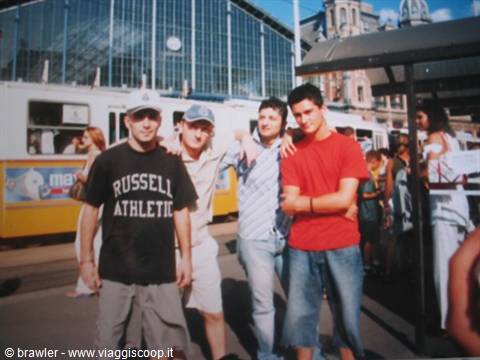 Four young men pose in front of a yellow tram and glass train station