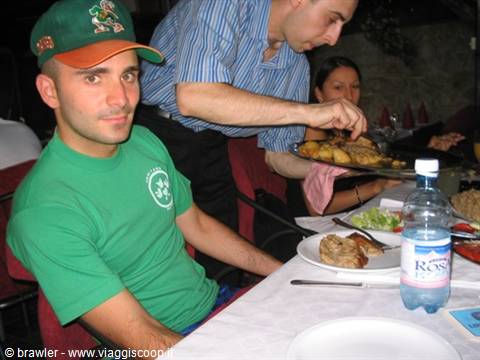 Waiter serving a tray of roast meat at a set table, man in green watching