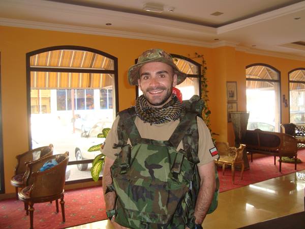 Smiling man in camouflage vest and hat inside a hotel with orange walls