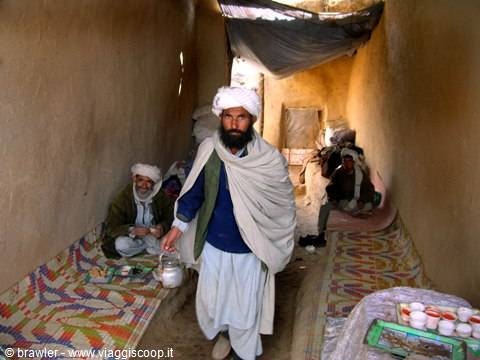 Man in white turban pours tea in an earthen room with carpets