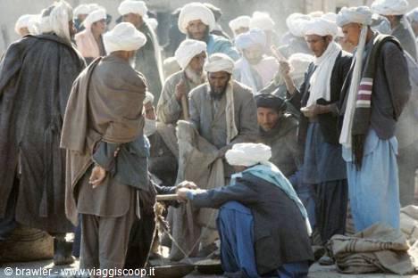 Men in white turbans gather around a weighing scale at an open-air market