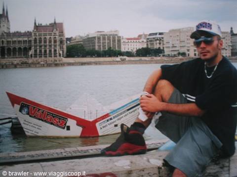 Young man sitting on the quay beside a Válasz boat, Budapest Parliament behind