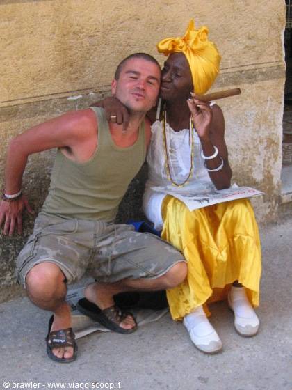 Cuban woman in yellow headscarf smokes a cigar beside a tourist