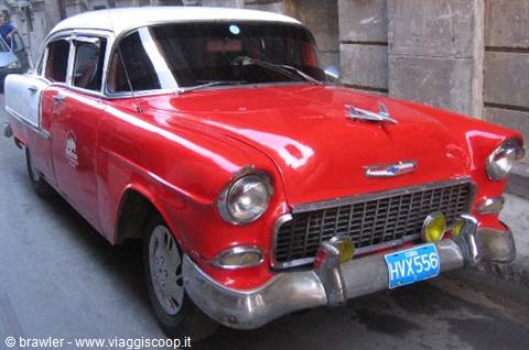 Red and white vintage Chevrolet parked beside an old stone wall