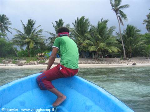 Boy in green shirt sitting on blue boat bow near palm-lined beach