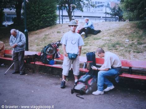 Backpacker with hat and gear beside red benches in a city park