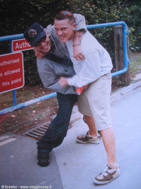 Two young men hugging and laughing beside a red sign on asphalt road