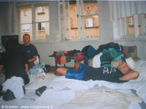 Young backpackers in a cluttered hostel room, clothes piled on beds