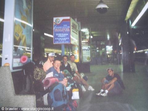 Backpackers with sleeping mats sitting on the floor of a railway station