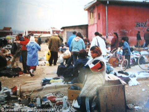 Secondhand market among red shacks, people rummaging through clothes and bicycles