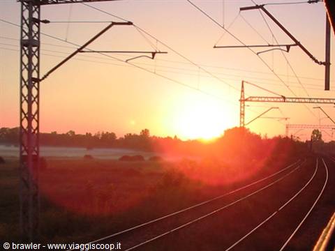 Sunrise over curving railway tracks, steel pylons and overhead wires backlit