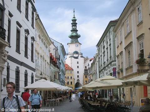 Tourists among café umbrellas on the street with St Michael's Gate in Bratislava