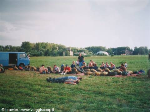 Group of people sitting on grass beside a blue van, open field
