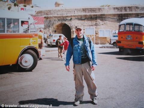 Traveler in denim jacket among colorful vintage buses in front of the fortified gate