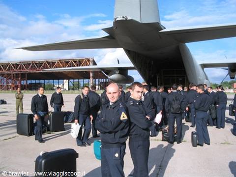 Uniformed soldiers with luggage gathered under a military cargo aircraft's tail