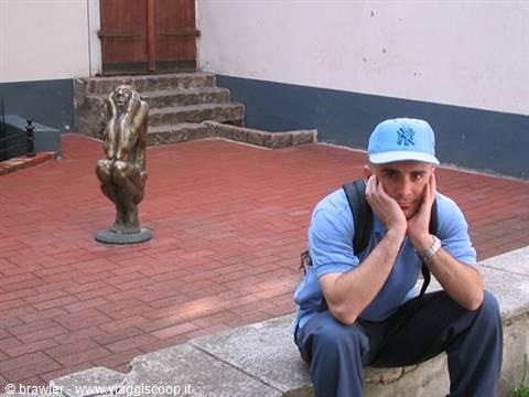 Tourist in blue cap sitting beside a bronze statue on red bricks