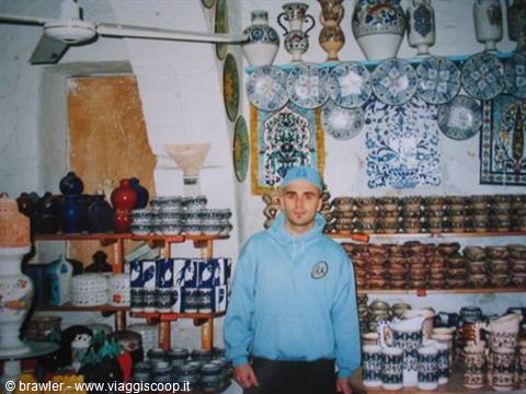 Young vendor in blue sweatshirt among hand-painted ceramics and decorated plates