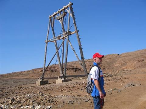 Tourist in red cap beside an old wooden mining headframe in the desert