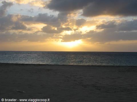 Low sun behind clouds over the ocean, dark sandy beach in the foreground