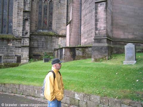 Man in yellow jacket beside a Gothic stone cathedral and a gravestone