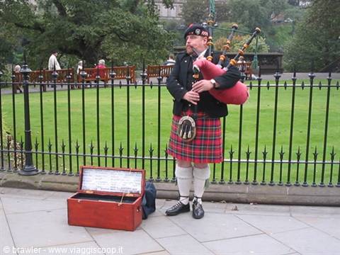 Bagpiper in tartan kilt playing beside an iron fence in Edinburgh park
