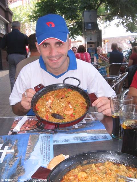 Tourist in blue cap shows a seafood paella pan at the restaurant