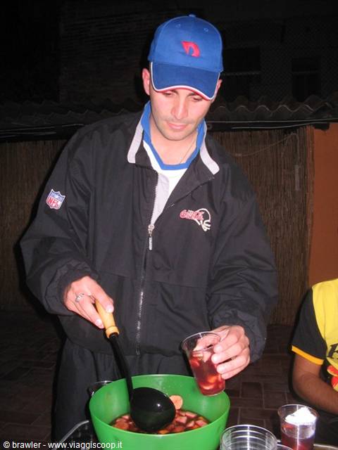 Man in blue cap ladles fruit and liquid into a glass