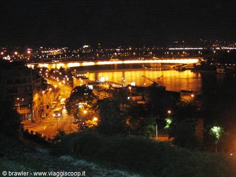 Night scene: river lit by an illuminated bridge, road with cars in foreground