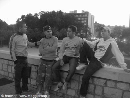 Four young men sitting on a stone wall in a city square at dusk