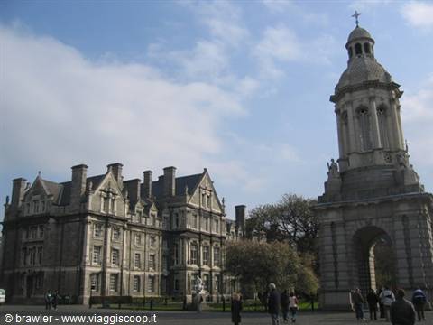 The stone bell tower and grey brick buildings of Trinity College, Dublin, under scattered clouds