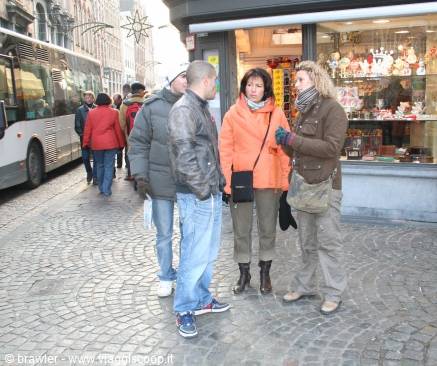 Four tourists chatting on cobblestones outside a shop, a bus behind