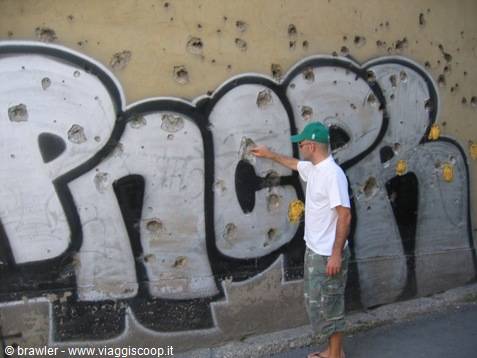 Man touches a graffiti wall riddled with bullet holes